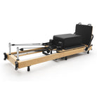Foldable Pilates Reformer Flexi, light wood, black upholstery – 3/4 view with sitting box