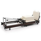 Foldable Pilates Reformer Flexi, dark wood, milky white upholstery – 3/4 view with sitting box